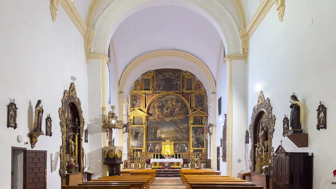 Single-nave Baroque church interior in Córdoba with a gilded Valdés Leal altarpiece filling the straight chevet, soft light falling on the painted canvases