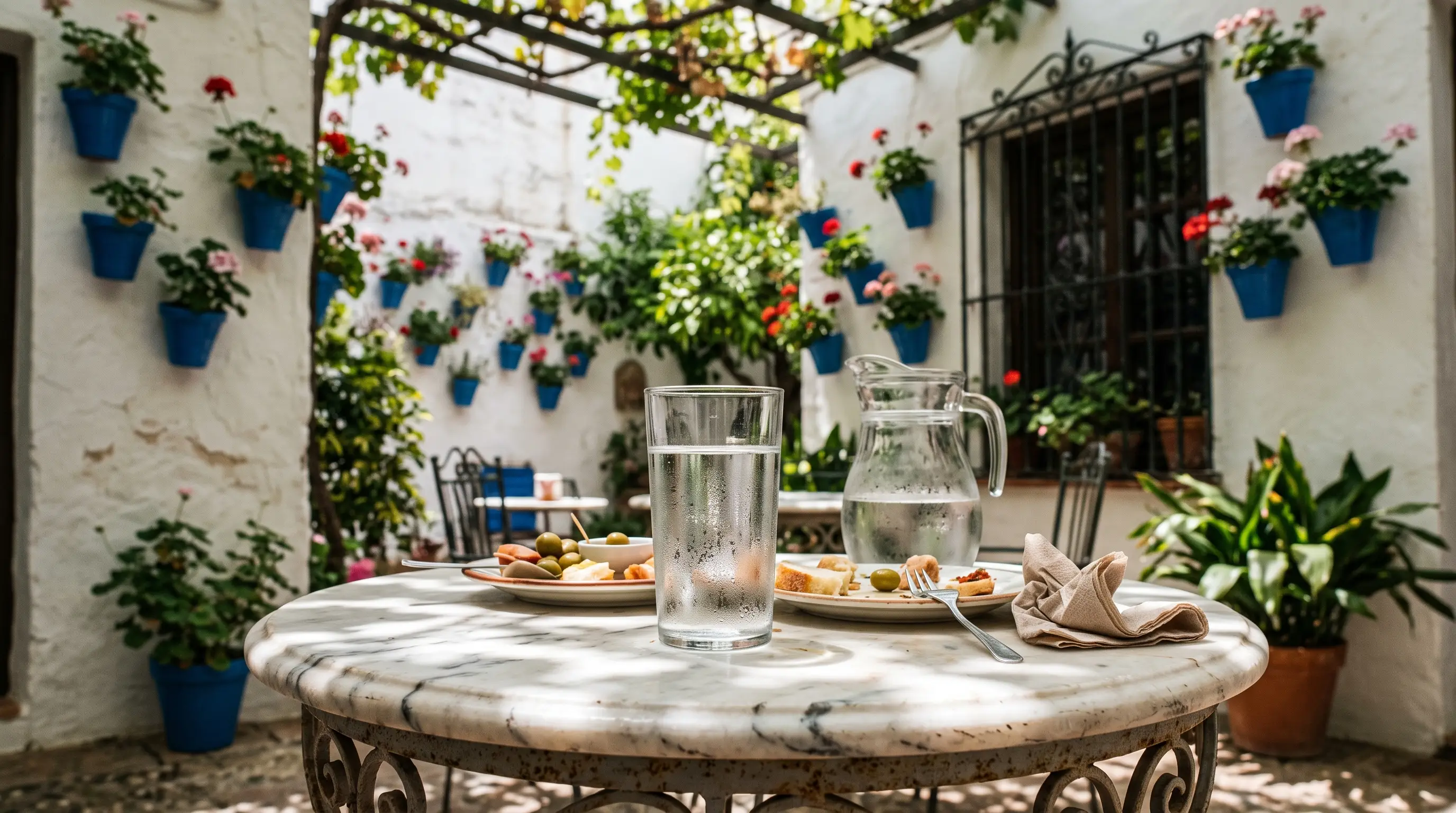 Glass of tap water on a café table beside a whitewashed Córdoba patio at midday, answering can you drink tap water in cordoba