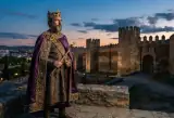 Illustration of Leovigild as a sixth-century Visigothic king in a purple mantle and gold crown, holding a sceptre, with the walls of Córdoba behind him at dusk